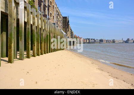 Clean firm stretch of beach sand River Thames shoreline below old riverside warehouse building on timber piles at Wapping Tower Hamlets East London UK Stock Photo