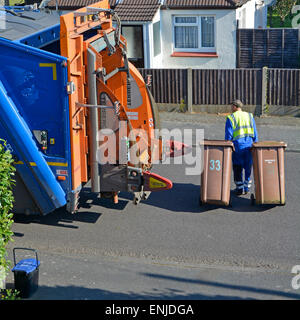 Back view from above high visibility dustman rear of refuse collection truck pulling two wheelie bins in residential street Brentwood Essex England UK Stock Photo