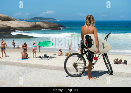 RIO DE JANEIRO, BRAZIL - FEBRUARY 2015: Brazilian surfer on a bike sits looking out at the waves at Arpoador. Stock Photo