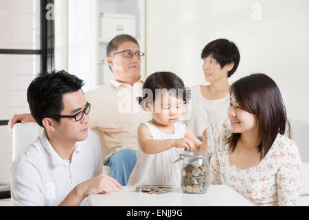 Toddler putting coins into money jar. Asian family money savings concept. Multi generations living lifestyle at home. Stock Photo