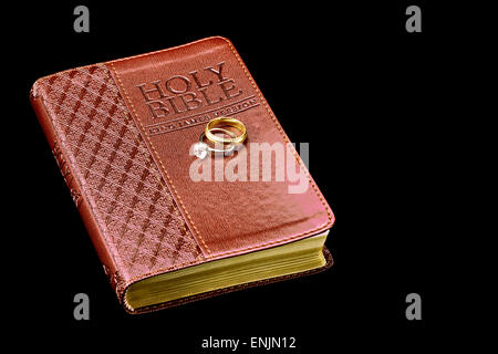 Holy Bible With Wedding Rings Isolated On Black Stock Photo