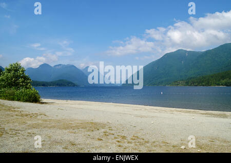 The sandy beach of Alouette Lake in Golden Ears Provincial Park.  Blue water and mountains on a sunny day.  In Maple Ridge, BC. Stock Photo