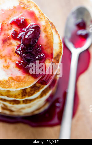 Cherry jam dripping from a stack of pancakes on the table and spoon Stock Photo
