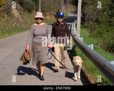 Older woman and man walking a yellow labrador retriever on a sunny day Stock Photo
