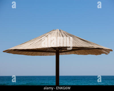 Upper part of a single sunshade made of straw against blue sky and sea. Stock Photo