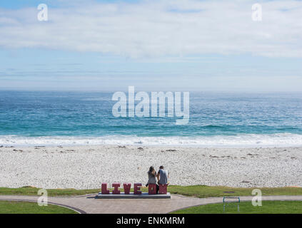 A couple at Camps Bay beach sitting on concrete letters spelling live on Stock Photo