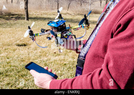 A 50 year old Caucasian man holds his Do It Yourself-built quadcopter drone,while looking at his mobile phone outdoors. USA. Stock Photo