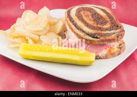 Classic reuben sandwich on pumpernickel swirl rye bread. A hearty meal with a side of pickle and chips Stock Photo