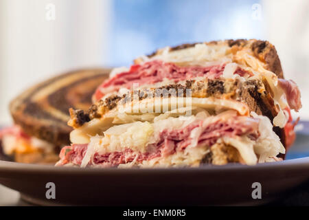 Classic reuben sandwich on pumpernickel swirl rye bread. A hearty meal with a side of pickle and chips Stock Photo