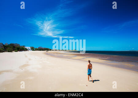 MANDA ISLAND, LAMU, INDIAN OCEAN, KENYA, AFRICA. A young woman walks down an empty white beach under bright blue sky. Stock Photo