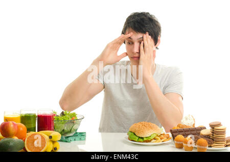 Man choosing between fruits, smoothie and organic healthy food against sweets, sugar, lots of candies and a big hamburger, fast  Stock Photo