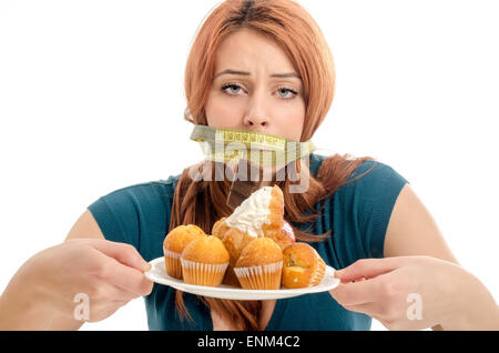 Woman with a centimeter on her mouth unable to eat all the sweets and sugar, lots of cookies on a plate. Dieting without sweets Stock Photo