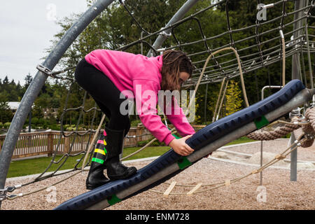 Young girl climbing up a swiveling board at a children's playground Stock Photo