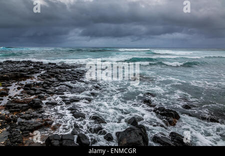 stormy ocean , dramatic sky. A storm sends waves over a rocky volcanic beach in Hawaii. Stock Photo