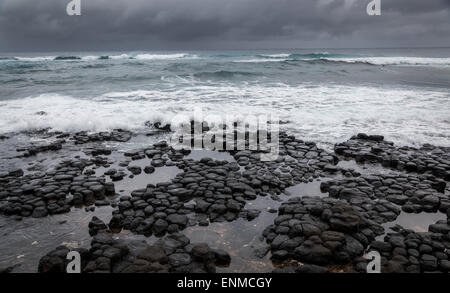 stormy ocean , dramatic sky. A storm sends waves over a rocky volcanic beach in Hawaii. Stock Photo