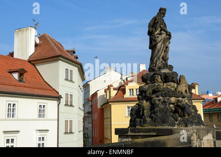 Statue of St. Vitus, one of famous sculptures of Charles Bridge on background of buildings of Lesser Town on corner of Near Lusa Stock Photo