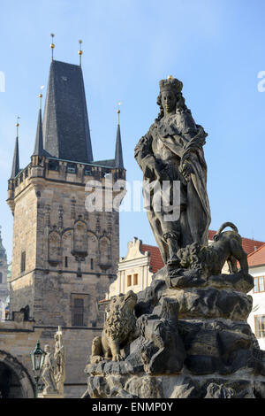 Statue of St. Vitus, one of famous sculptures of Charles Bridge with Gothic tower on the side of Lesser Town on background in Pr Stock Photo