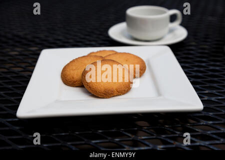 Selective focus on butter cookies on white plate with espresso visible in shallow depth of field. Stock Photo