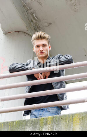 Attractive young man wearing black leather jacket looking down from balcony Stock Photo