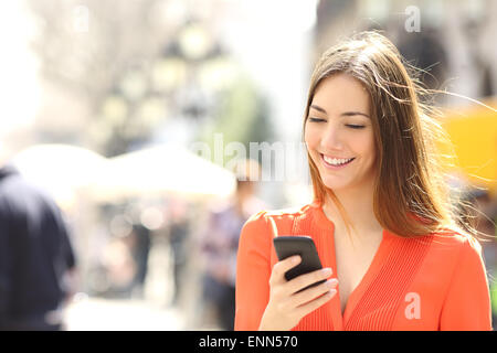 Woman wearing orange shirt texting on the smart phone walking in the street in a sunny day Stock Photo