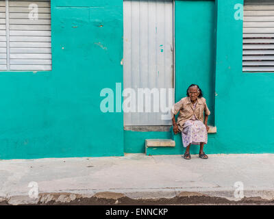 Afro-Cuban senior in doorway of aqua building looking unhappy in Santiago de Cuba. Stock Photo