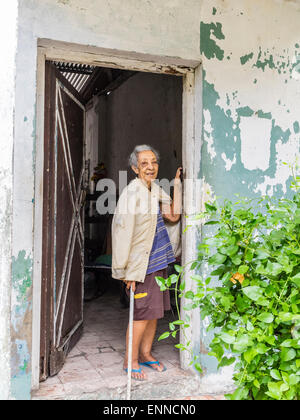 Female Afro-Cuban senior citizen with gray hair standing in the doorway of her house looking out, one arm up against the doorway Stock Photo