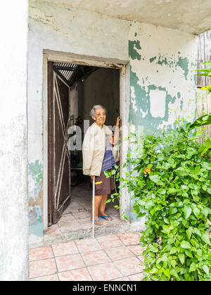 Female Afro-Cuban senior citizen with gray hair standing in the doorway of her house looking out, one arm up against the doorway Stock Photo