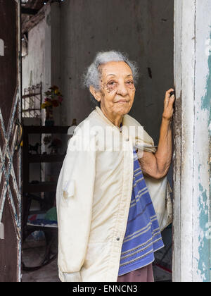 Female Afro-Cuban senior citizen with gray hair standing in the doorway of her house looking out, one arm up against the doorway Stock Photo