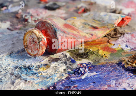 Closeup of old oil paint tube with red colour lying on dirty artistic palette ,background for creative art design Stock Photo