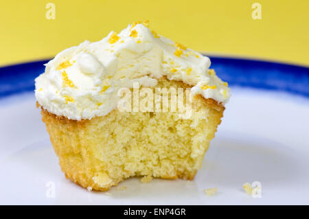 Lemon cupcake with a bite taken out of, on a white and blue plate and a yellow background Stock Photo