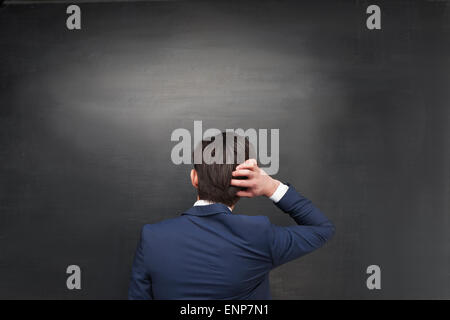 Back photo of pensive businessman on chalkboard background Stock Photo