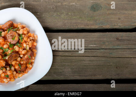 Baked beans and sausages in white plate over wood background with copy space Stock Photo