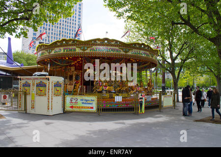 People walking past a colorful carousel in central London, United Kingdom. Sunny weather and green leaves on trees. Stock Photo