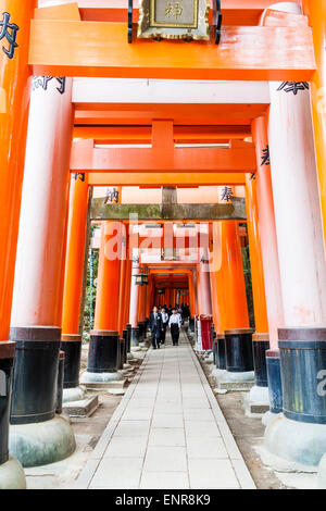 View along corridor formed by row of vermilion, orange, torii gates at the famous Fushimi Inari-Taisha shrine in Kyoto. Group of salarymen at end. Stock Photo
