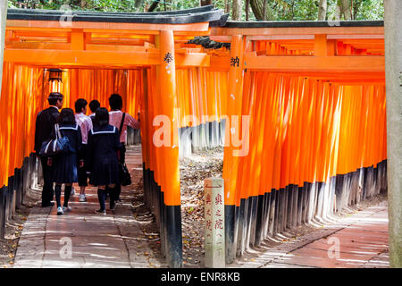 Schoolgirls walking through a double corridor formed by hundreds of vermilion, orange, torii gates at the famous Fushimi Inari-Taisha shrine in Kyoto. Stock Photo