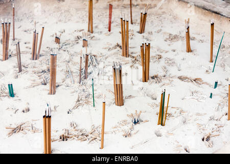 Incense sticks stuck in a sea of white ash in an incense burner at a Japanese shrine/temple. Sticks left single or in little groups of three. Stock Photo