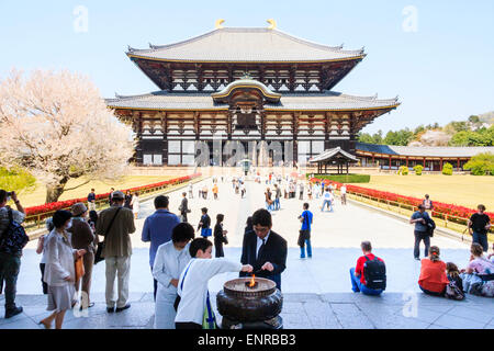 The Todai-ji temple at Nara, Japan. In foreground an Asian family lit incense sticks in large incense burner. Behind them, the great hall, Daibutsuden. Stock Photo