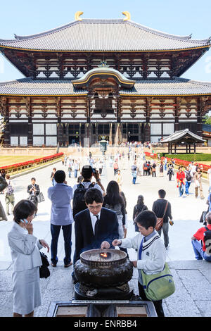 The Todai-ji temple at Nara, Japan. In foreground an Asian family lit incense sticks in large incense burner. Behind them, the great hall, Daibutsuden. Stock Photo