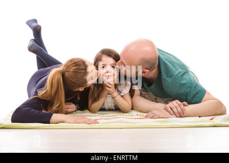 Parents laying on blanket in a row and kissing their daughter Stock Photo