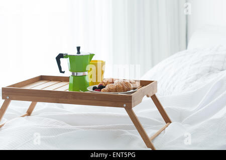 Breakfast wooden tray with coffee percolator and croissant on bed Stock Photo