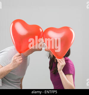 couple kissing and hiding behind heart shaped balloons. copy space available Stock Photo