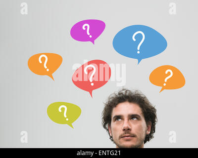 thinking man with many question marks in bubbles above his head, against grey background Stock Photo