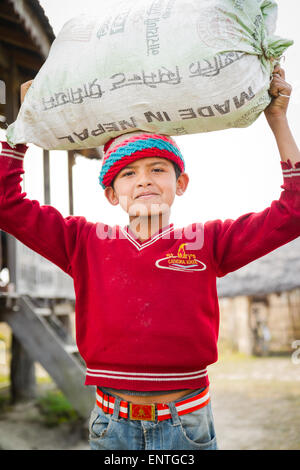 Young boy of Tharu ethnicity carrying a large sack in rural east Nepal Stock Photo