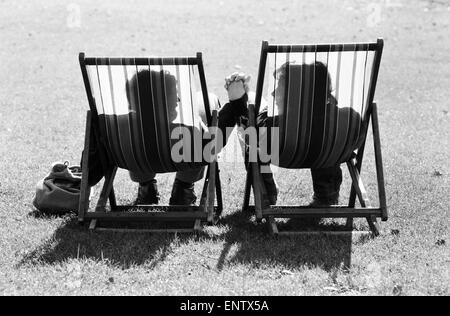 A couple in sit in a pair of deckchairs holding hands and looking at one another as they enjoy the warm spring sunshine. 4th March 1979. Stock Photo