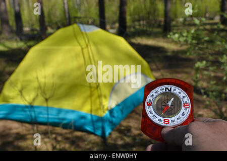 Compass and tourist tent. The magnetic compass in the hand against the tent in the forest in spring. Stock Photo