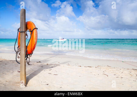 Red round life buoy hanging on wooden pole, empty sandy beach of Dominican republic Stock Photo