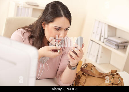 Young businesswoman applying lipstick at office Stock Photo