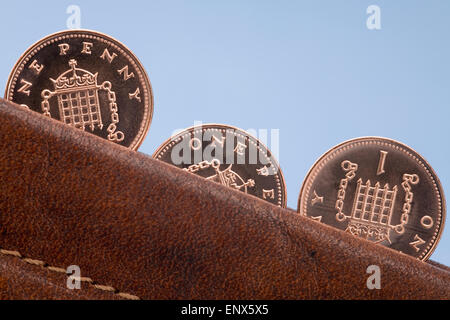 Three copper penny coins in close up sticking out from leather purse on blue. England UK Britain Stock Photo