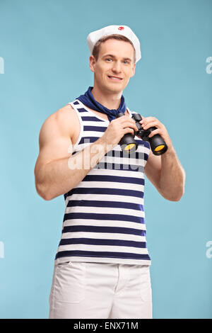 Vertical shot of a young male sailor holding binoculars and looking at the camera on blue background Stock Photo