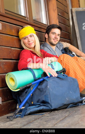 Tramping young couple backpack relax by cottage Stock Photo